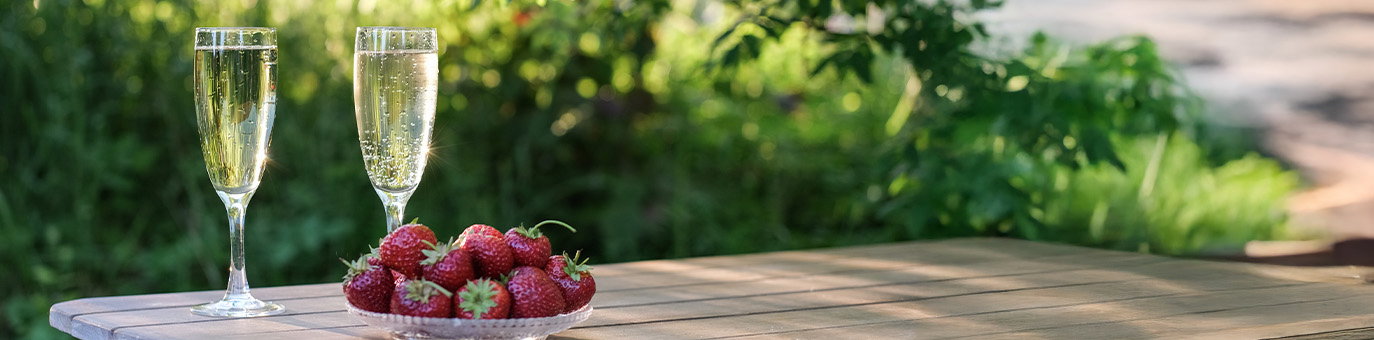 Sekt und Secco mit frischen Erdbeeren auf sommerlichem Gartentisch
